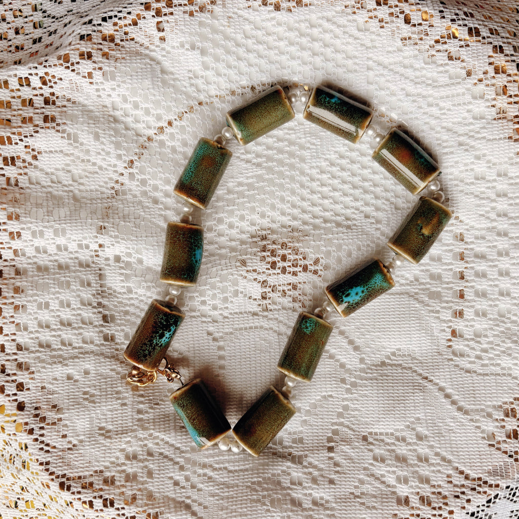 Necklace with green and gold stones on a lace background