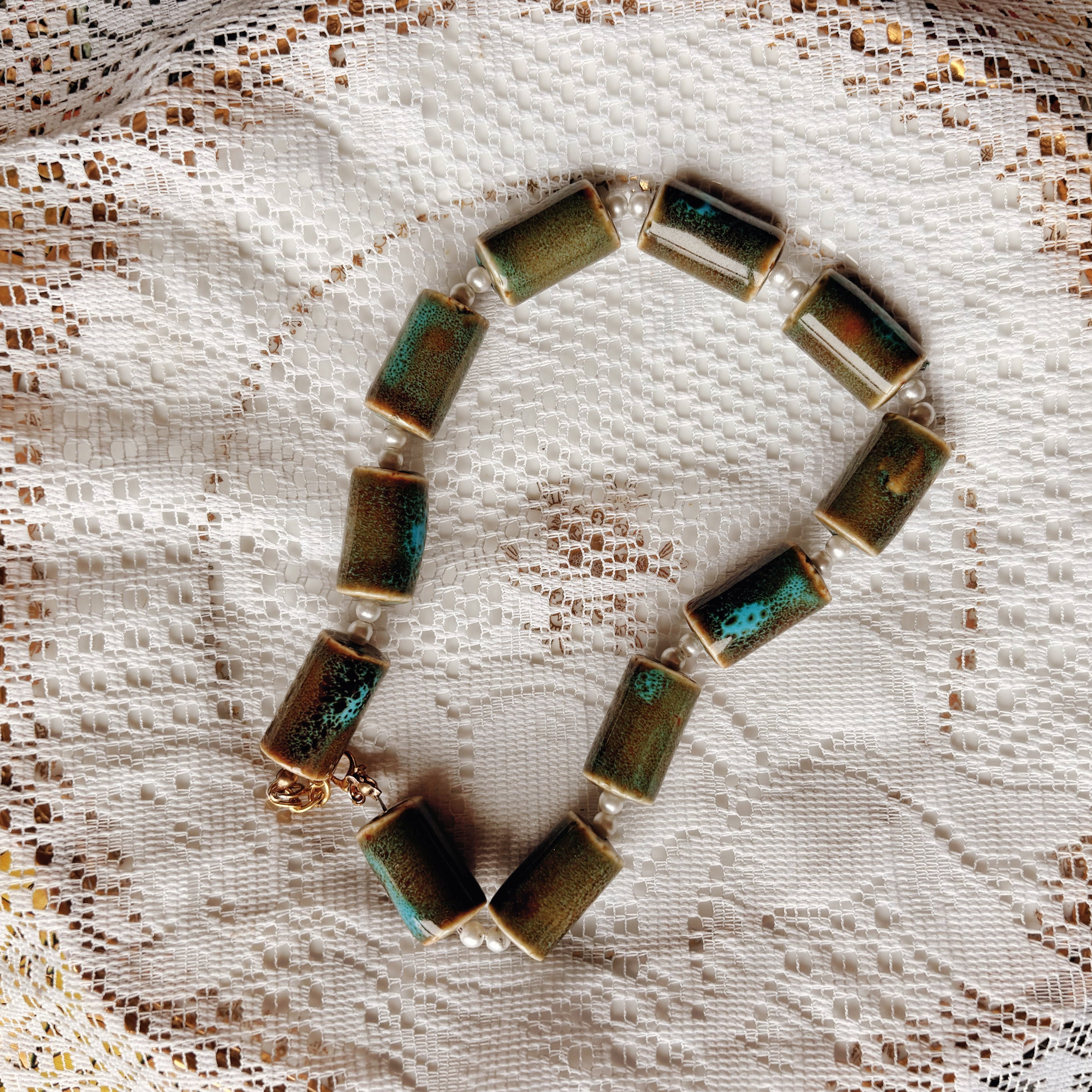 Necklace with green and gold stones on a lace background