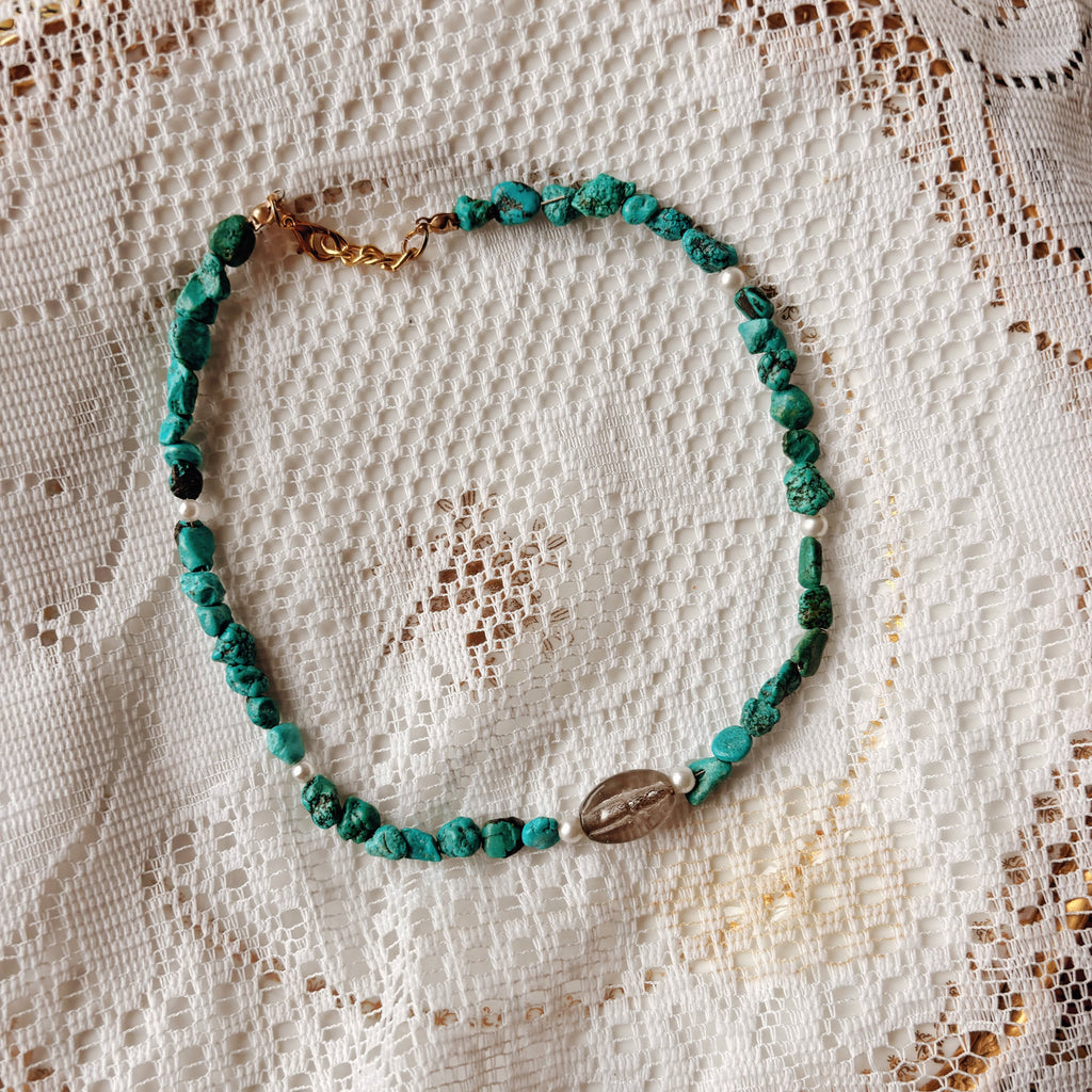 Turquose beaded necklace on a textured white fabric background