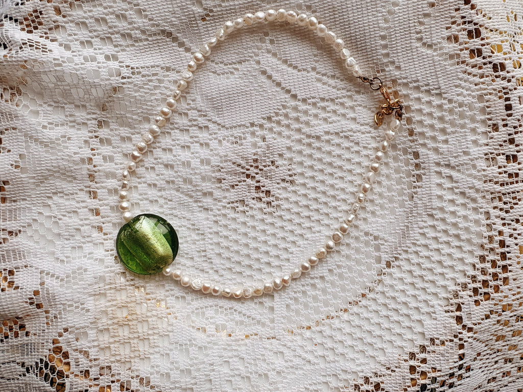 Pearl necklace with a green pendant on a lace background