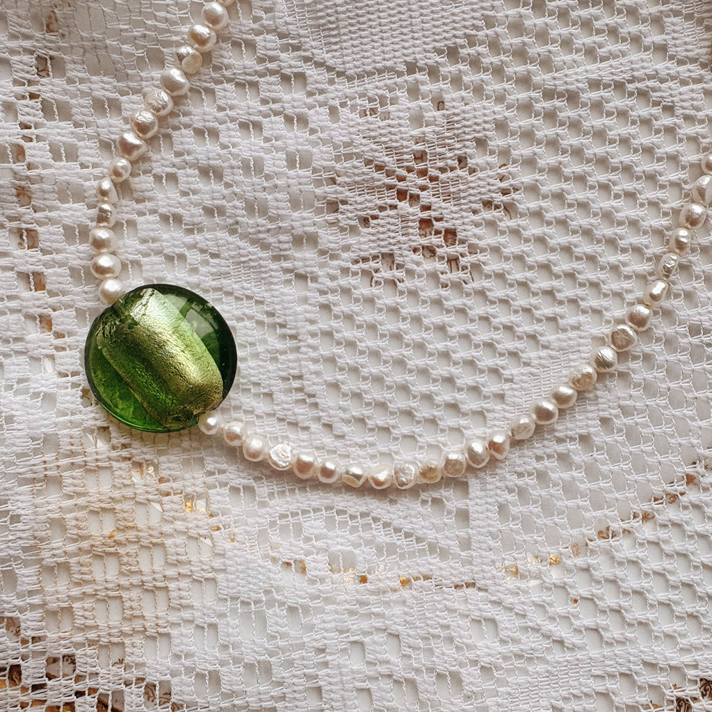 Pearl necklace with a green pendant on a lace background