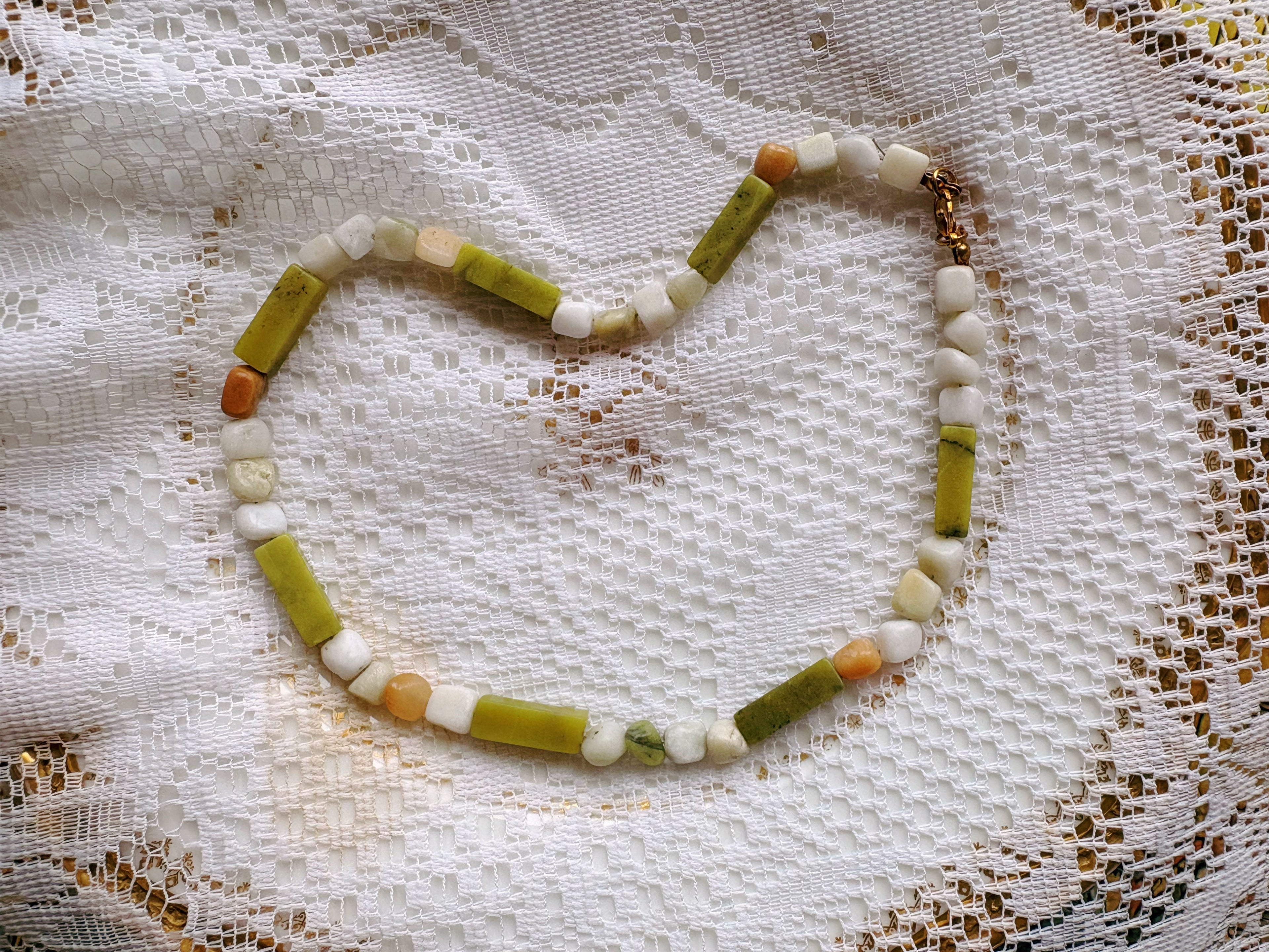 Necklace with green, white, and orange beads on a textured fabric background