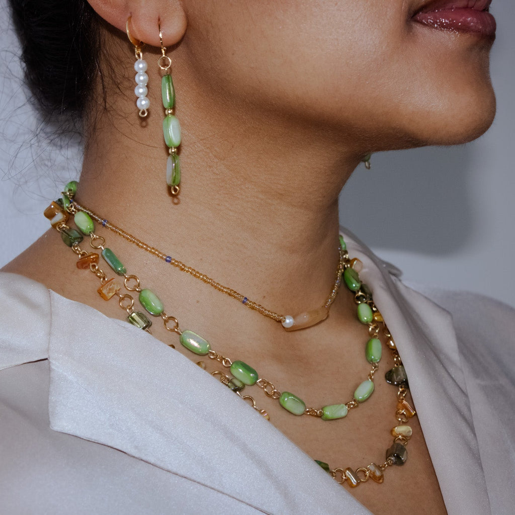 Close-up of a person wearing green and gold necklaces and earrings against a neutral background