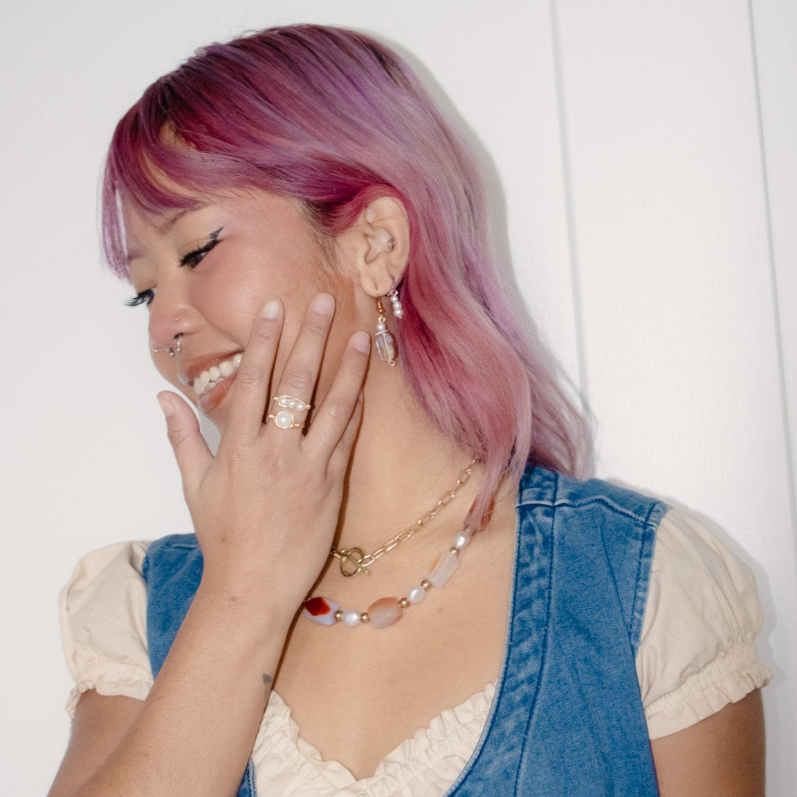 Woman with pink hair wearing a denim vest and white top, smiling.