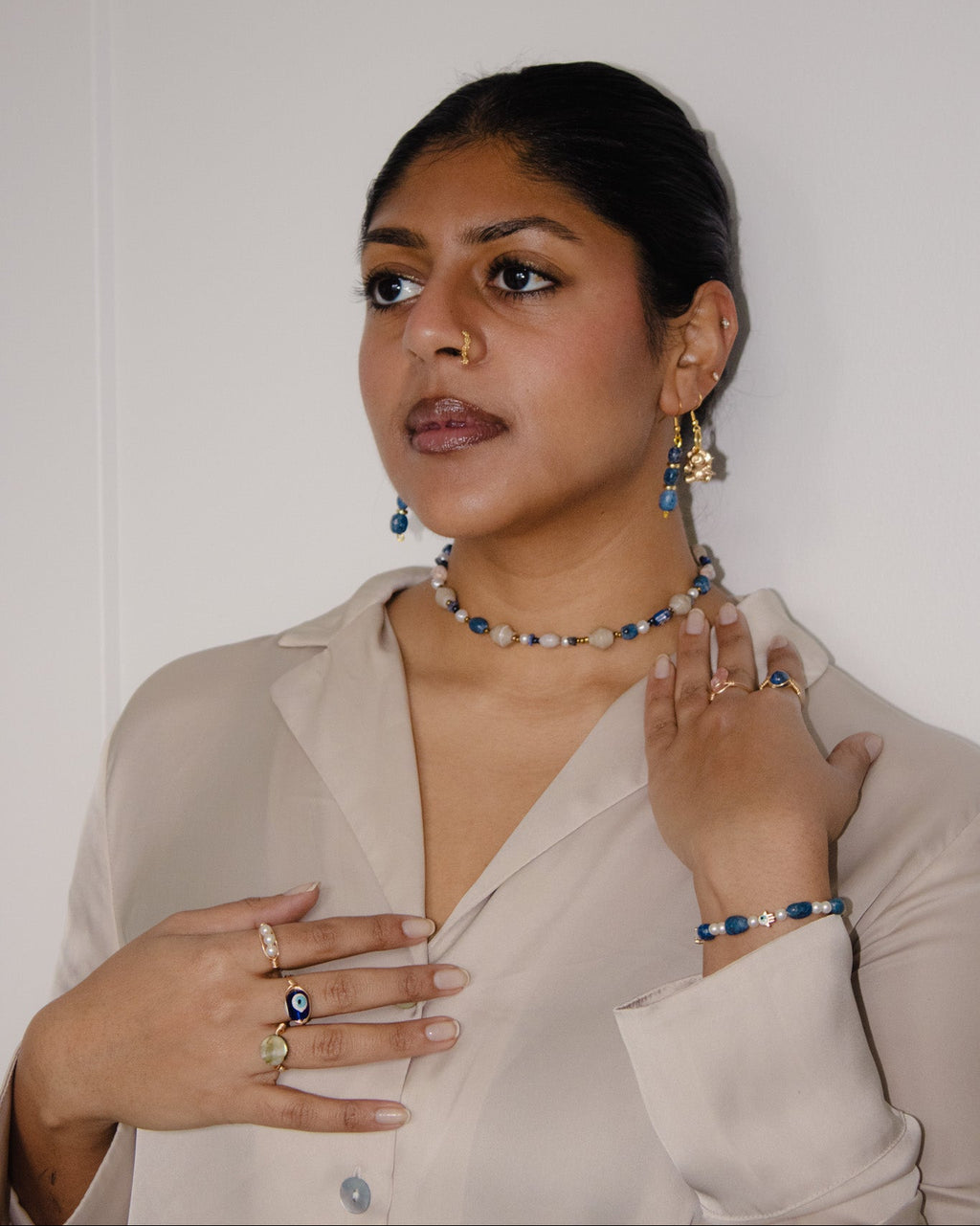 Woman wearing a beige blouse with jewelry against a plain background