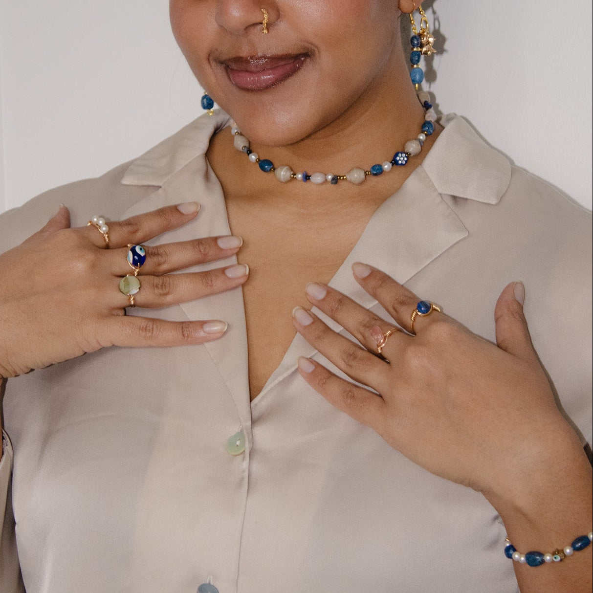 Woman wearing jewelry including a necklace, earrings, and rings against a plain background