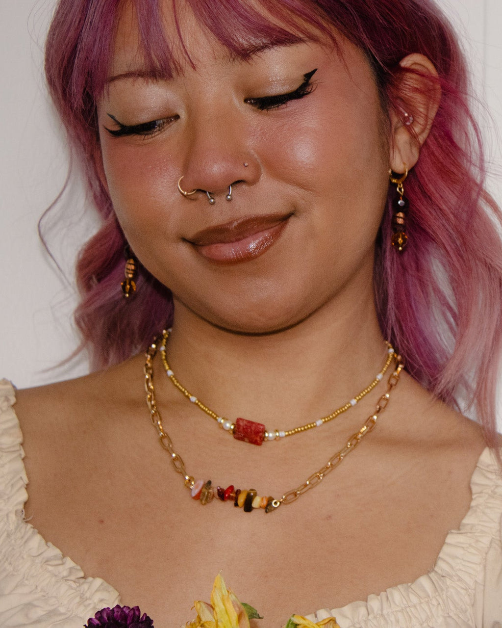 Person with pink hair wearing a gold necklace with colorful beads against a white background