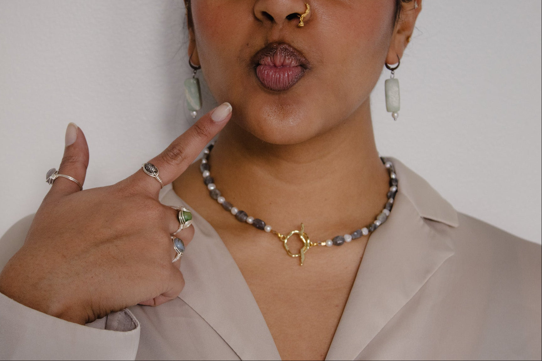 Woman wearing jewelry, including a necklace and rings, against a plain background.
