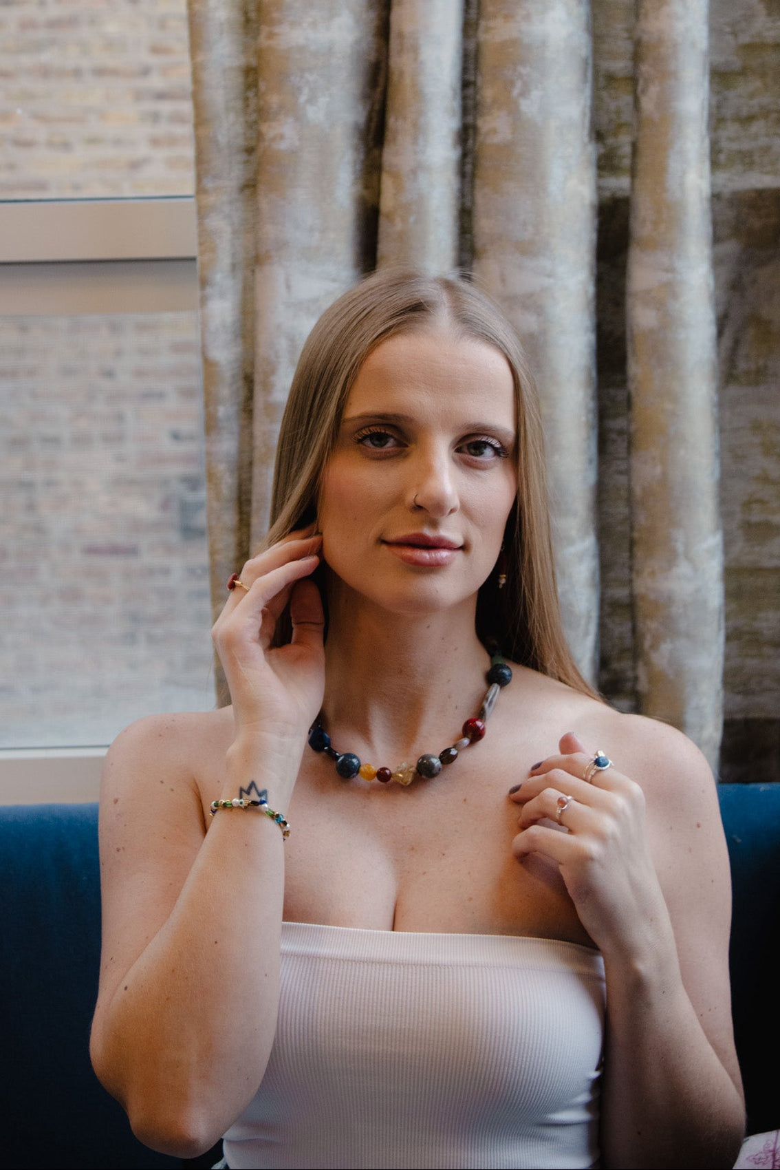 Woman wearing a necklace in an indoor setting with curtains and a window.