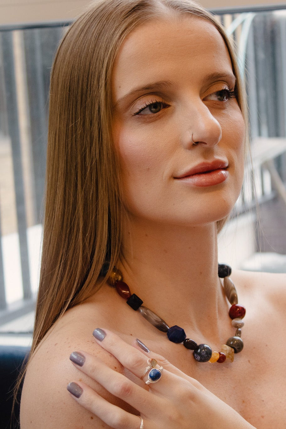 Woman wearing a colorful beaded necklace indoors with a blurred background