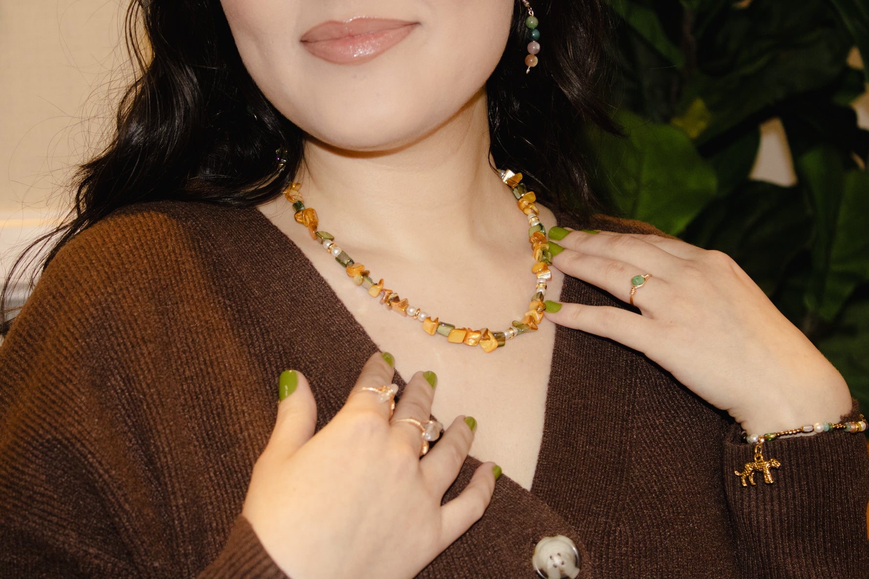 Woman wearing a necklace with a brown sweater and green nail polish.
