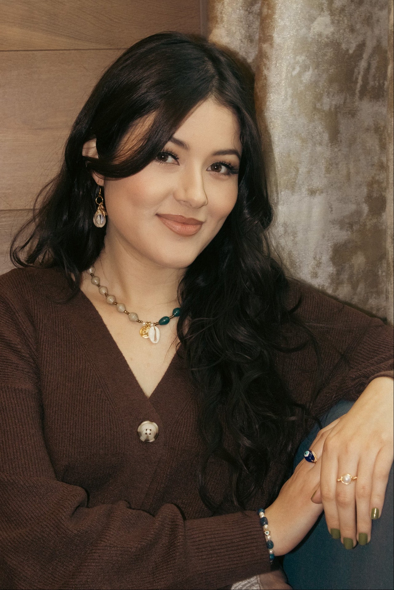 Woman wearing a brown sweater with jewelry against a wooden background