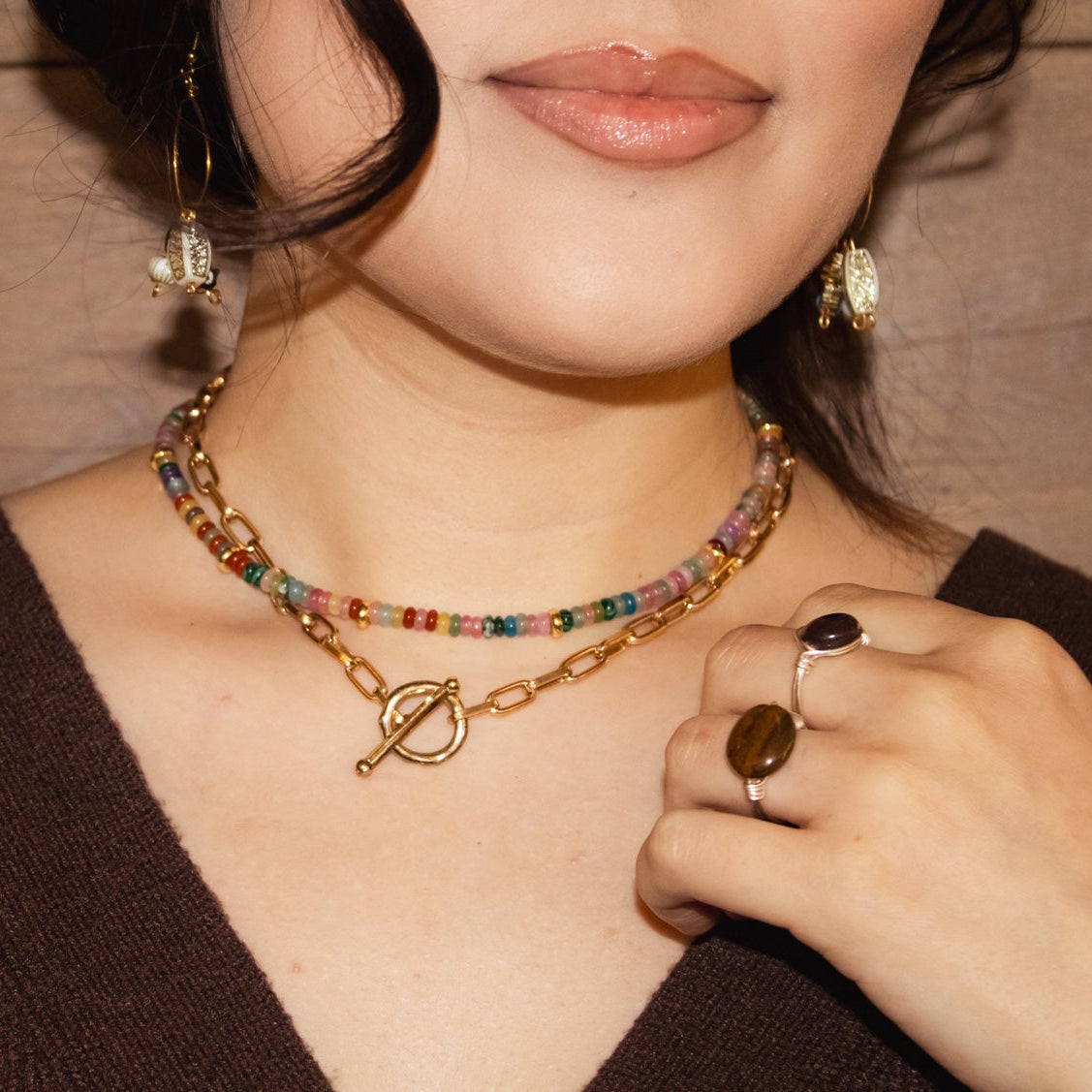 Close-up of a person wearing a colorful beaded necklace and rings against a wooden background