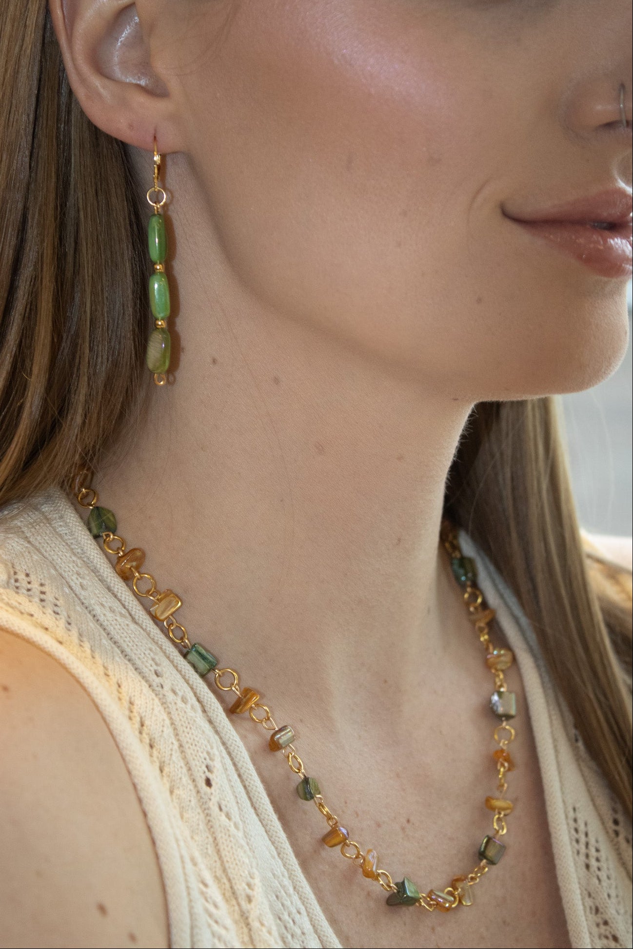 Close-up of a woman wearing a necklace and earrings with green and gold beads.