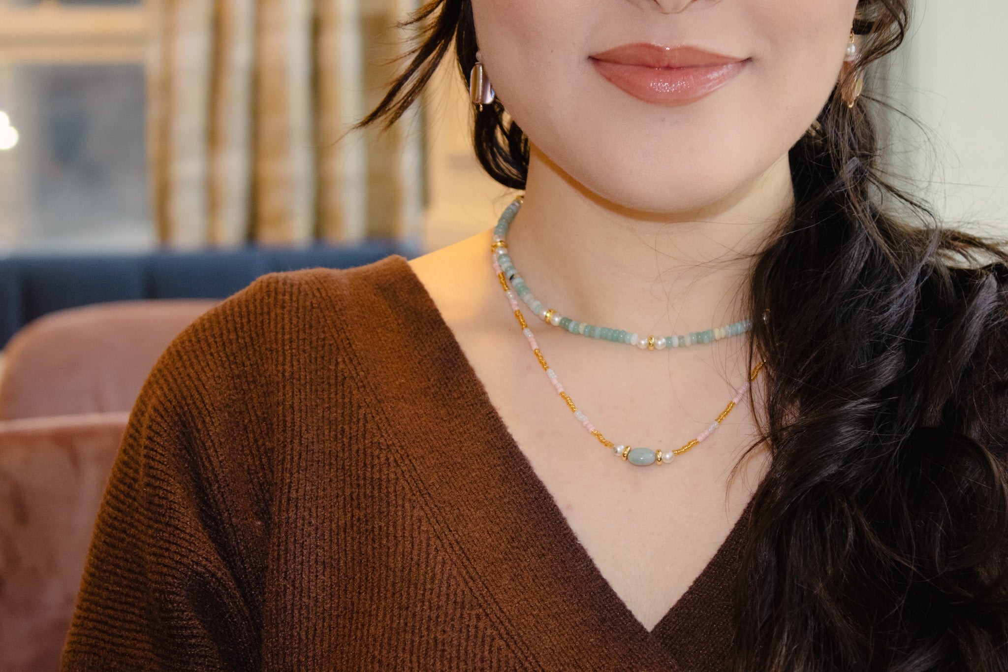 Woman wearing a brown sweater and multiple necklaces with a blurred background