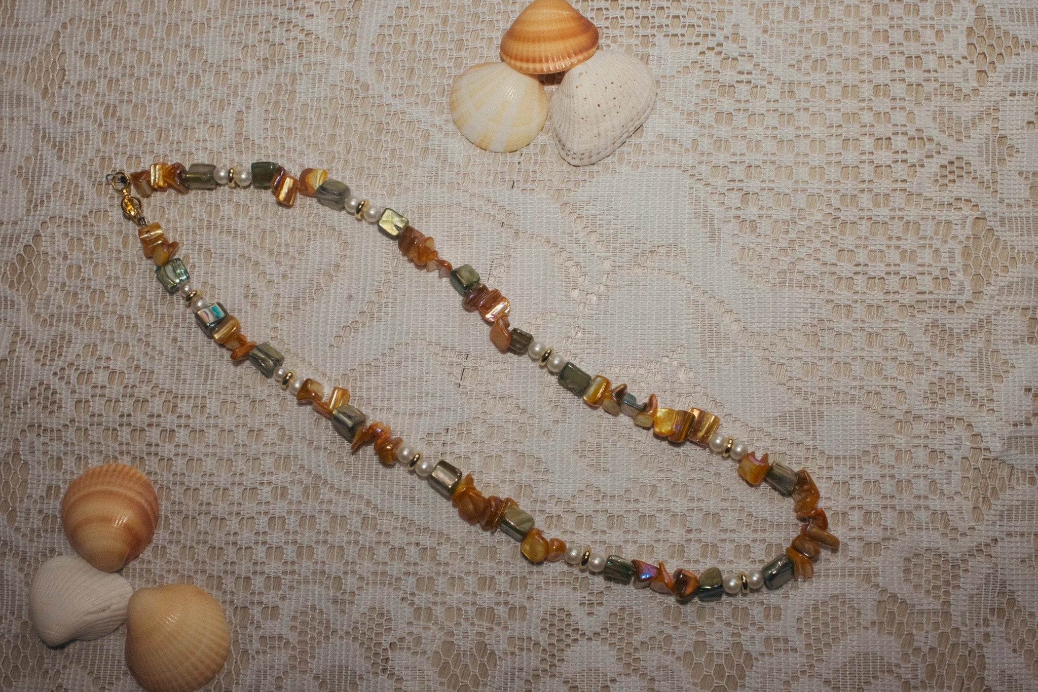 Necklace with multicolored beads on a lace tablecloth with shells.