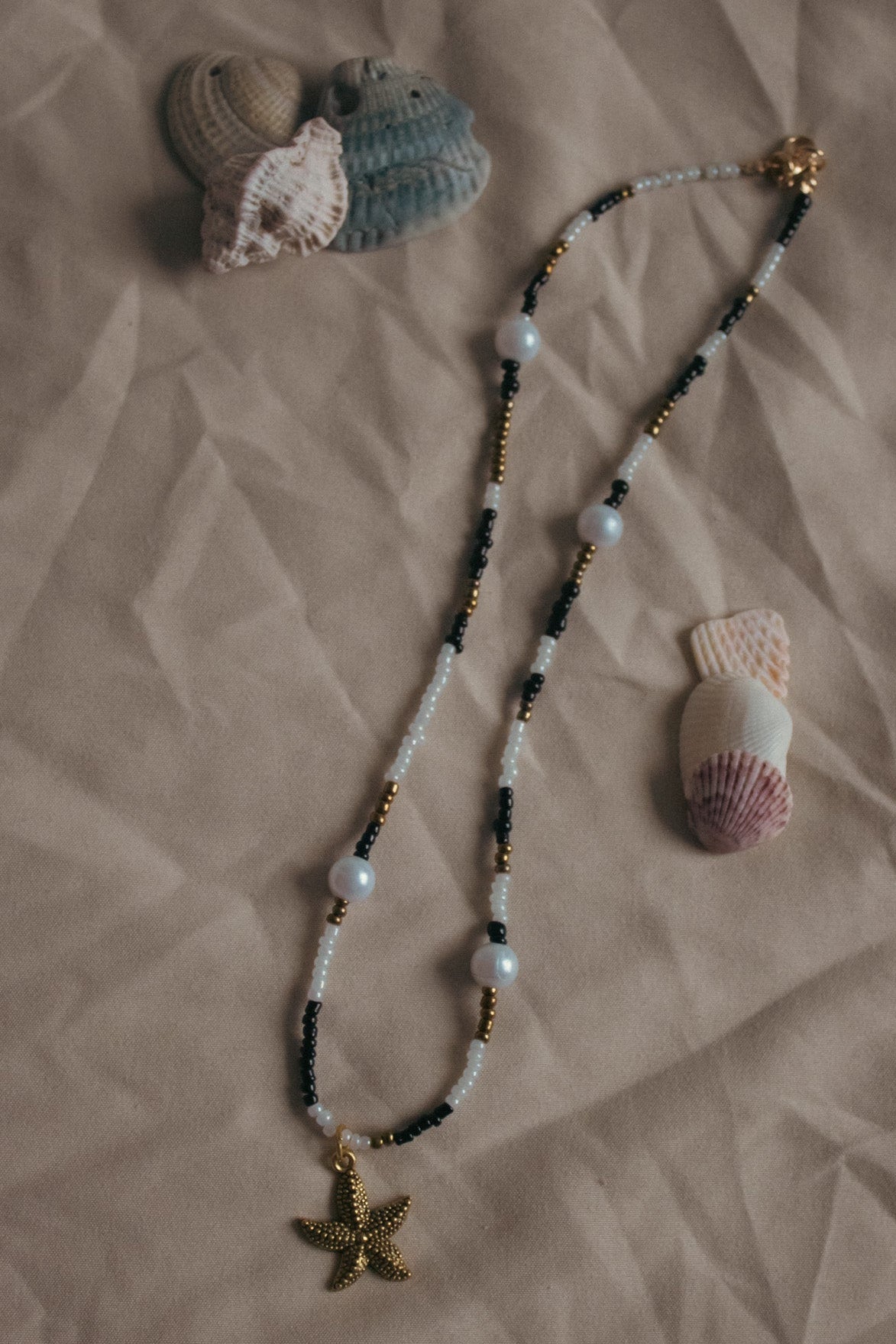 Necklace with starfish charm and seashells on a textured beige surface