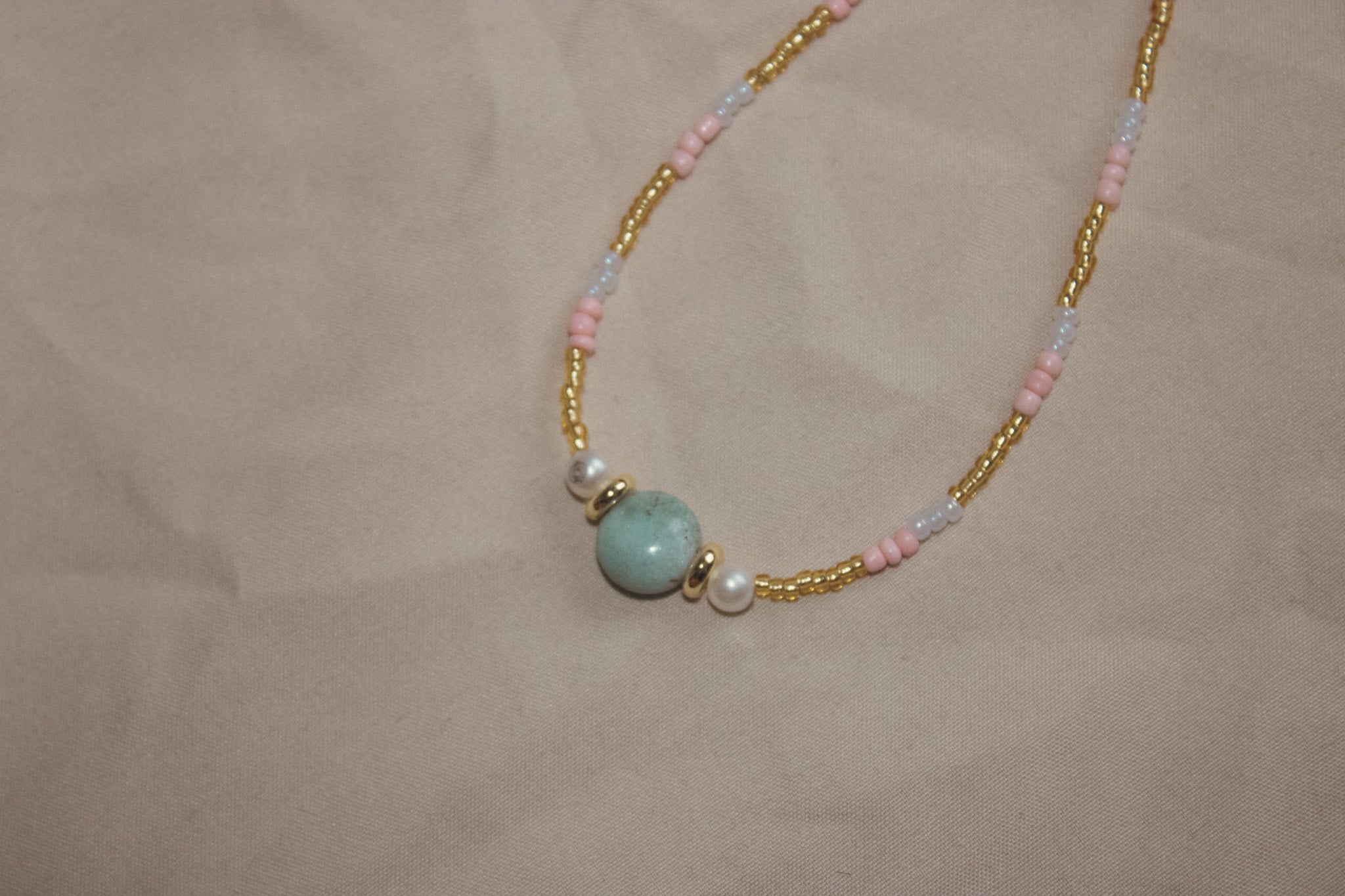 Necklace with gold chain, pink beads, and a turquoise bead on a beige background