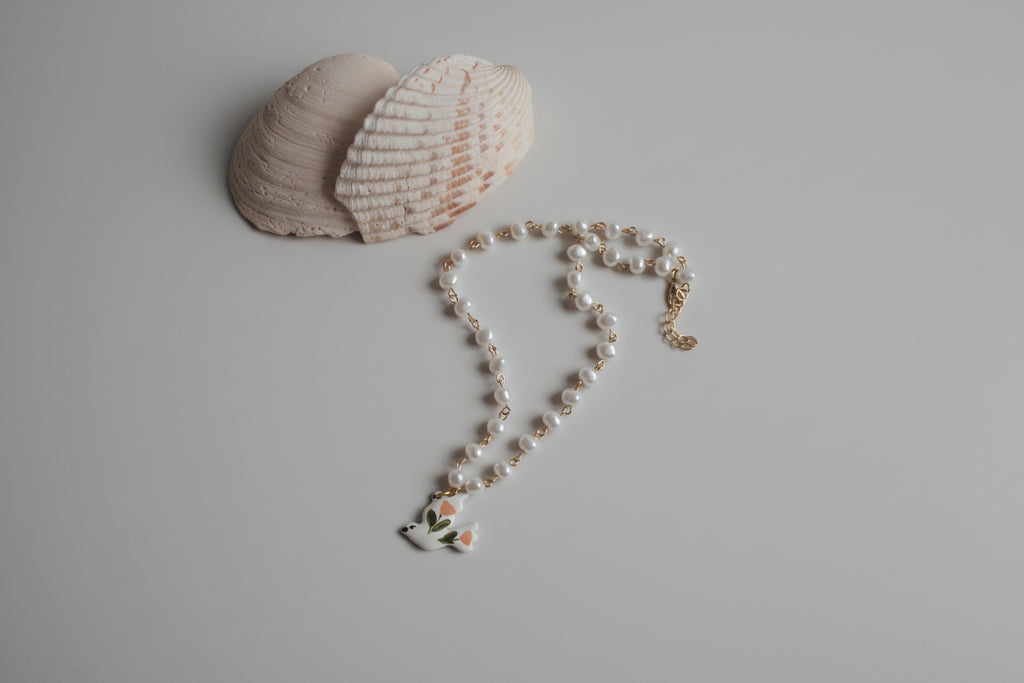 Pearl necklace with a bird charm on a textured surface with shells.