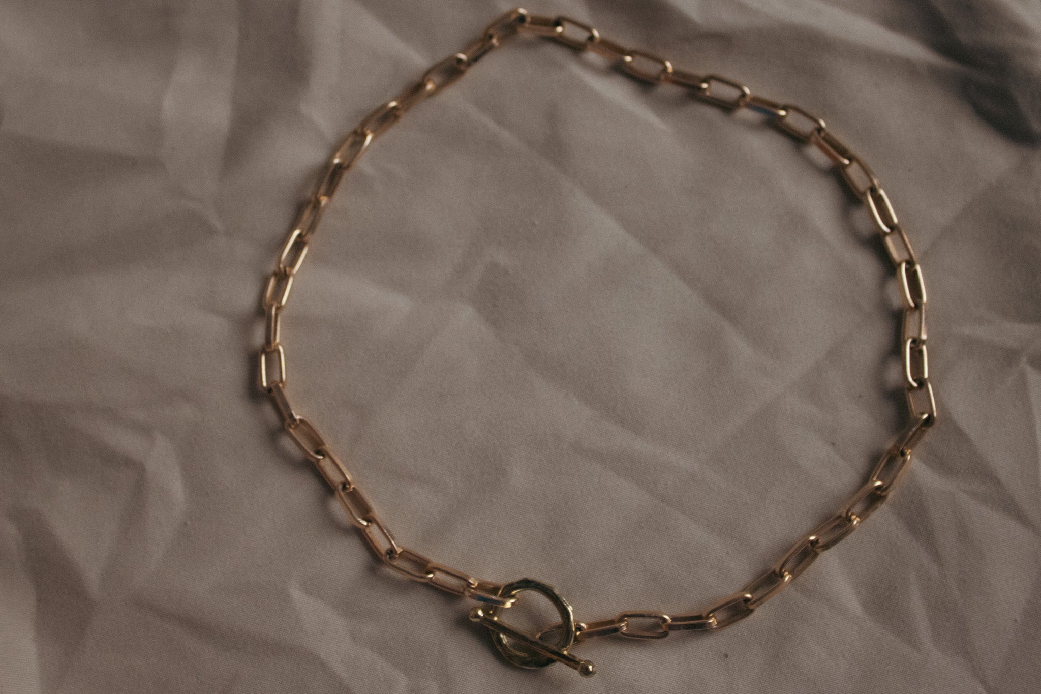 Gold chain bracelet on a textured beige background