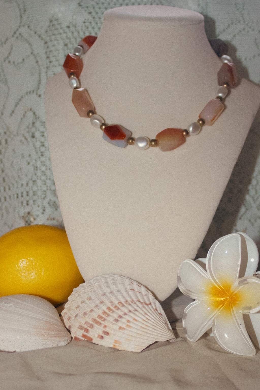 Necklace on a mannequin bust with a lemon, shell, and flower in front
