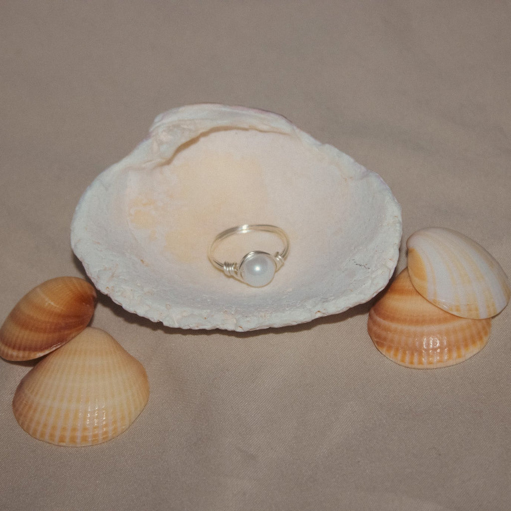 Pearl ring in a white shell surrounded by smaller shells on a beige background