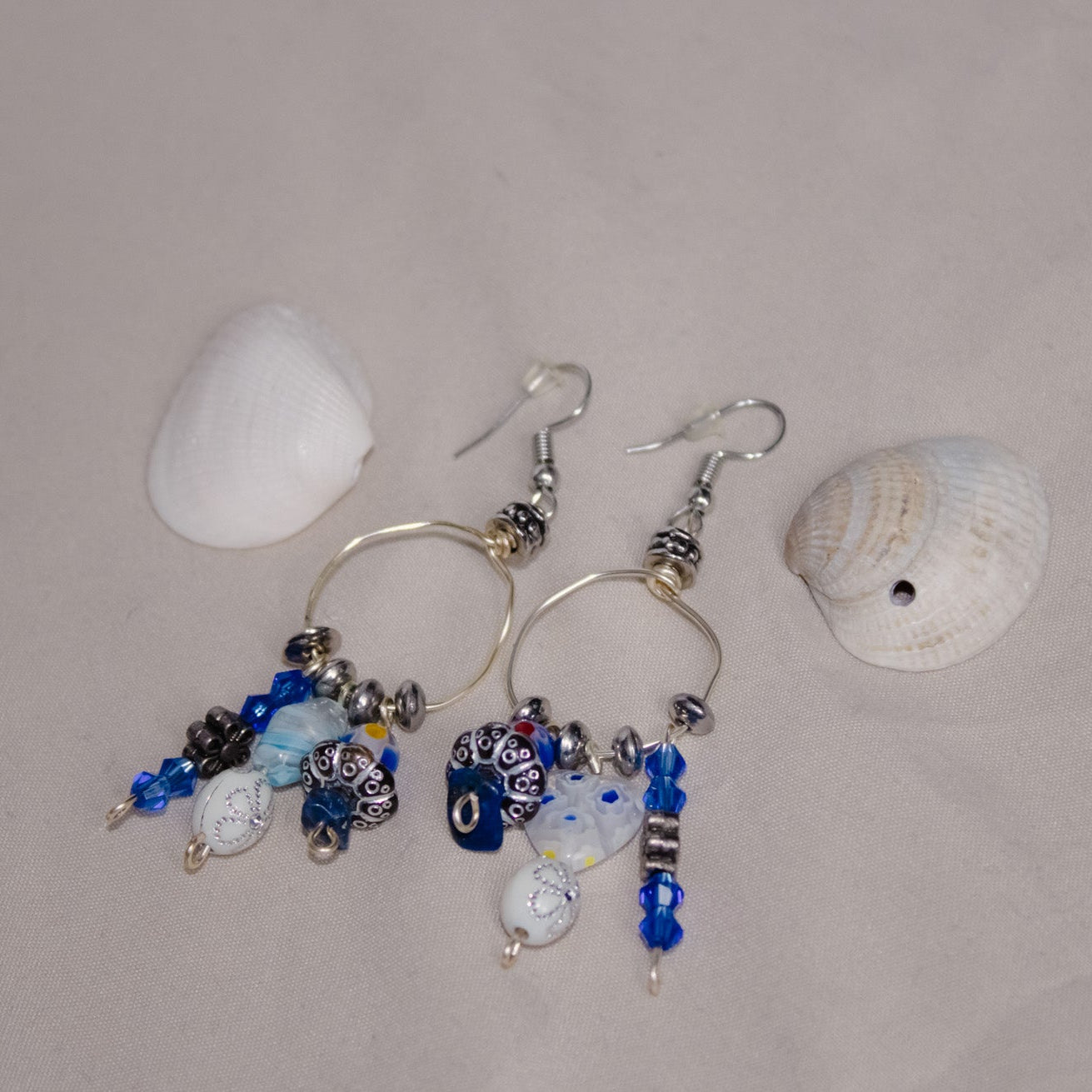 Beaded earrings with blue and silver beads on a beige background with two seashells.