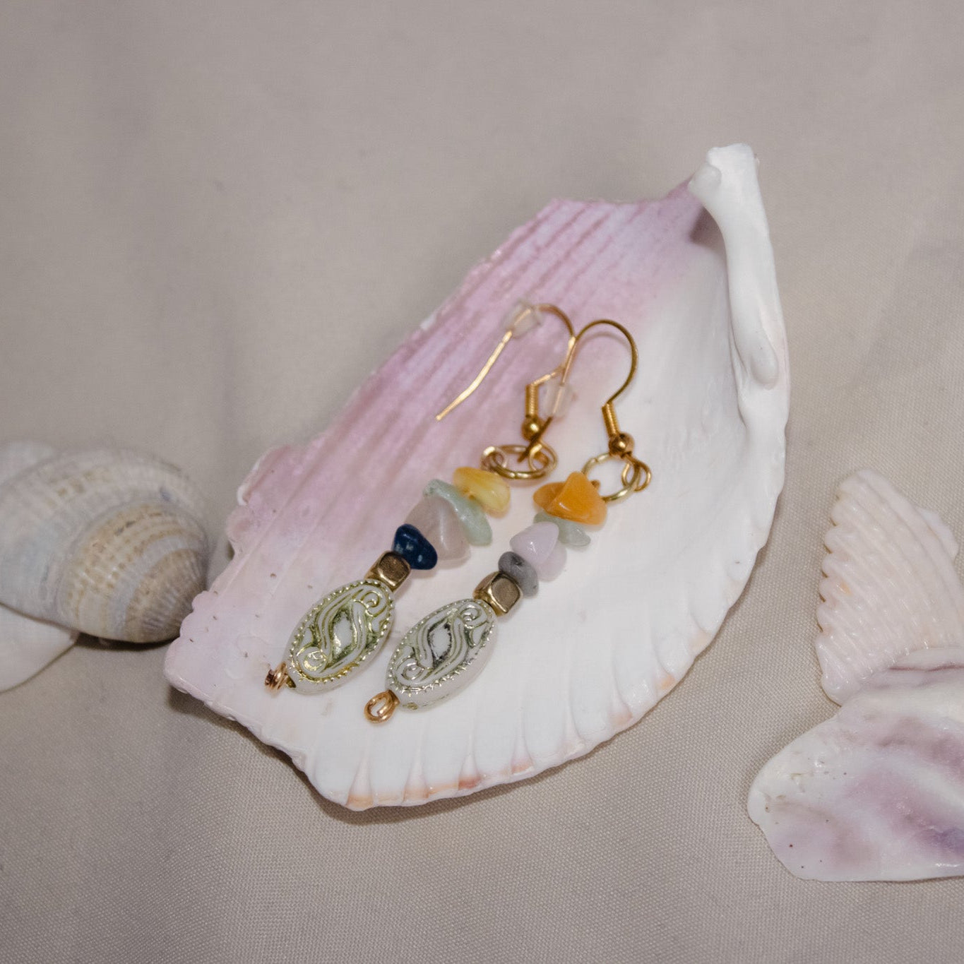 Pair of earrings with decorative charms on a seashell against a neutral background