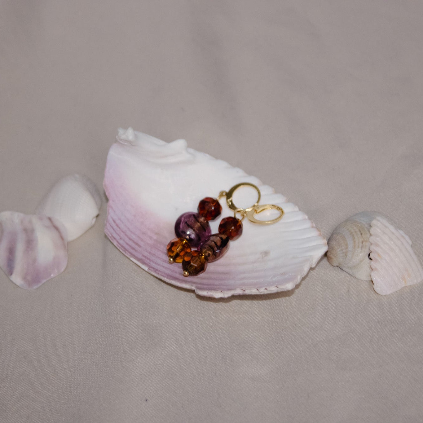 Jewelry set with beads and gold chain on a shell against a beige background