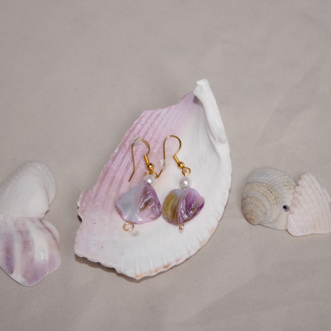 Pair of earrings with purple stones on a pink shell with additional shells on a beige background