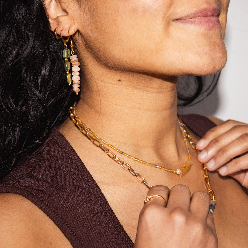 Woman adjusting a gold necklace with a neutral background