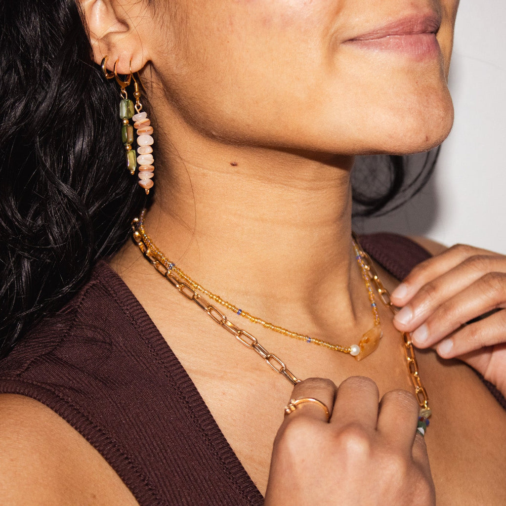 Close-up of a person wearing a gold chain necklace and earrings.