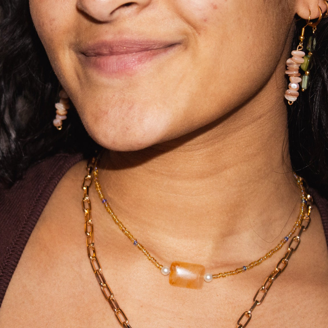Close-up of a person wearing layered necklaces and earrings with a neutral background