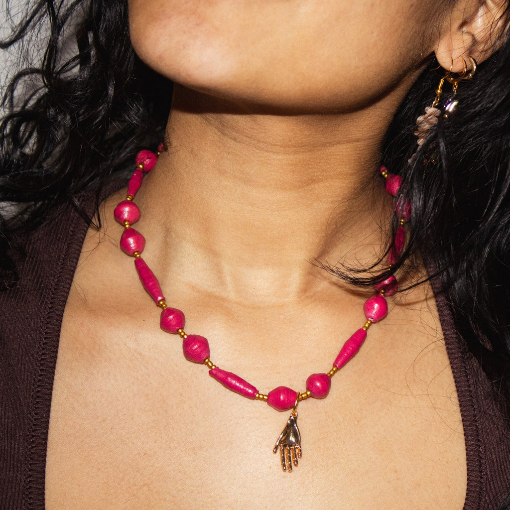 Close-up of a person wearing a pink beaded necklace with a hand charm.