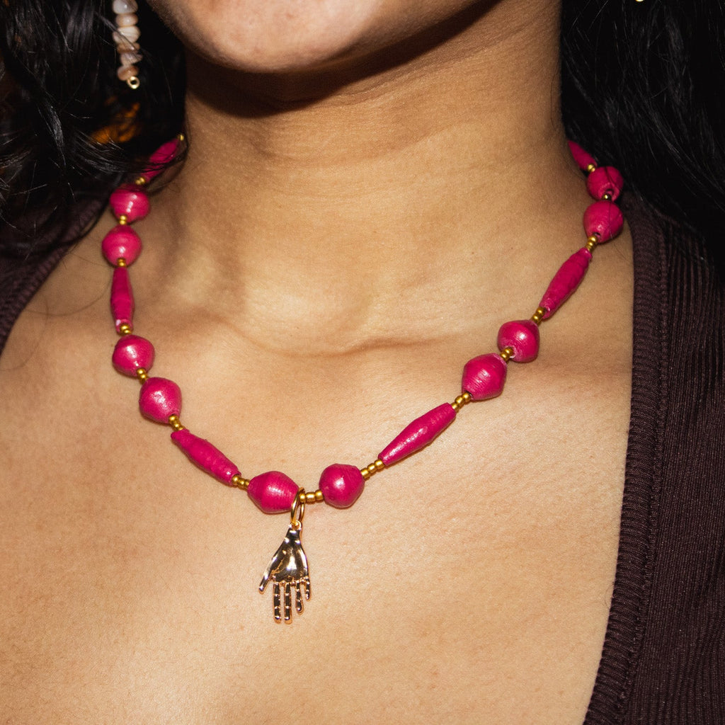 Close-up of a pink beaded necklace with a hamsa hand pendant on a person.