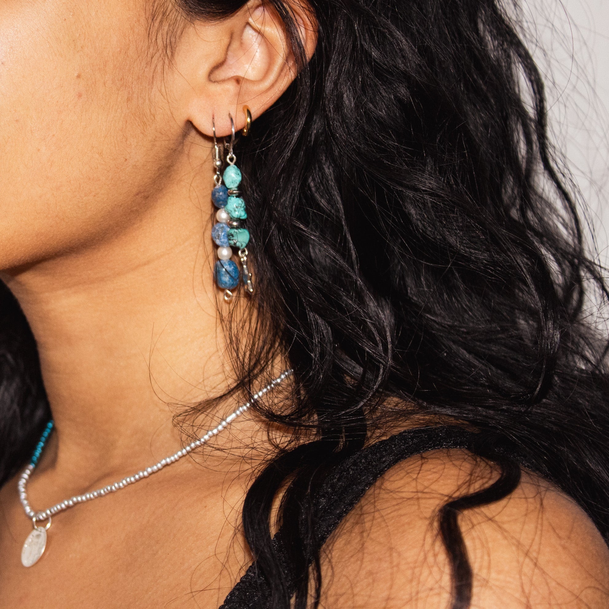 Close-up of a person wearing blue beaded earrings and a necklace with a blurred background